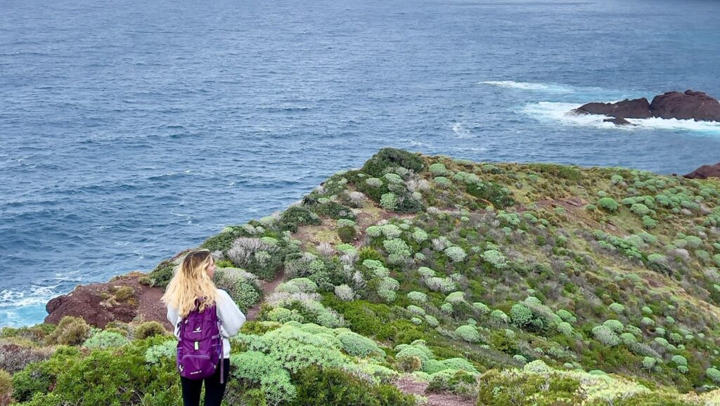 Frau mit Rucksack blickt aufs Meer beim Wandern.
